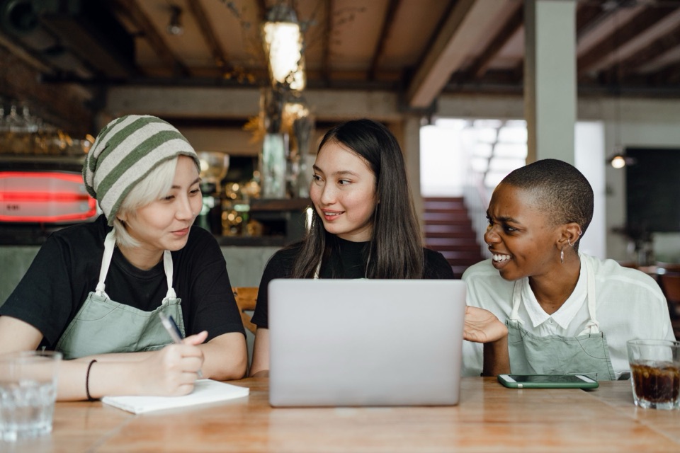 Three small-business owners smiling together at a laptop in their café
