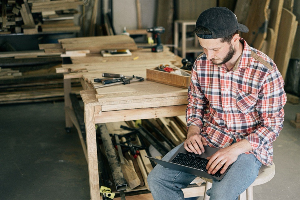A carpenter working on a laptop in his woodworking shop